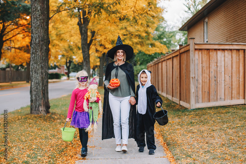 Trick or treat. Mother with children going to trick or treat on Halloween holiday. Mom with kids boy and girl in party costumes with baskets going to neighbour houses for candies, treats.