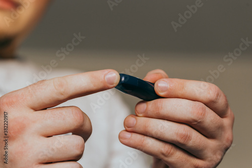 Medicine  diabetes  glycemia  healthcare and people concept - close up of a man s hands using a lancet on his finger to check blood glucose meter with copy space for text