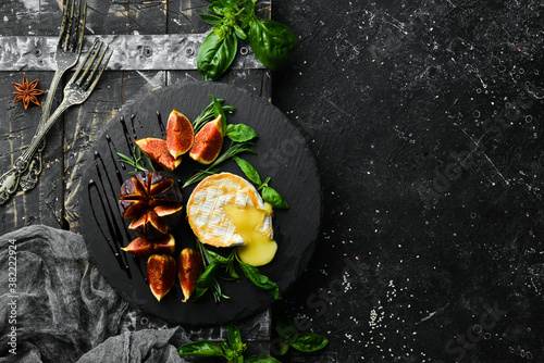 Grilled brie cheese with figs and basil on a black stone plate. Top view. Free space for your text.