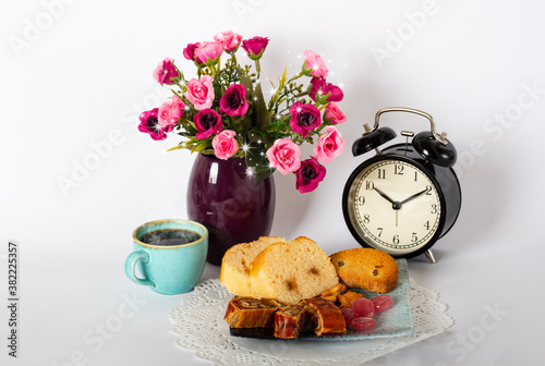 Breakfast composition with cup of black coffee with alarm clock, dessert and beautiful purple flowers in vase on a white background. Healthy food concept with copy space. Studio shot. Banner.