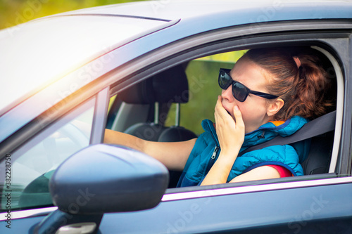 A woman drives a car, a woman in a traffic jam in sunglasses, yawns covering her mouth. Fall asleep while driving an automobile
