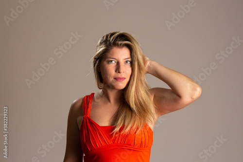 Portrait of young blonde woman smiling with raised arm and hand in hair. Brazilian in neutral background. Empowered and happy.