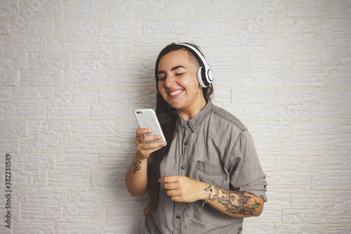 Cool girl with sidecut hairstyle is reading good news on mobile phone. Technology, social media, connection concept. Neutral, gray colors. photo