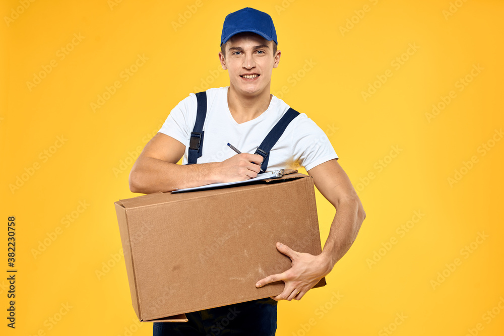 Working man in uniform with box hand delivery loading service yellow background Working man in uniform with box hand delivery loading service yellow background