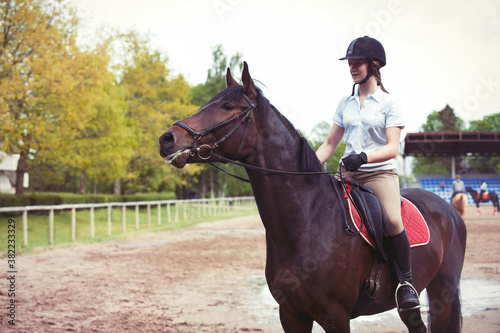 Cheerful teenage girl equestrian riding chestnut horse