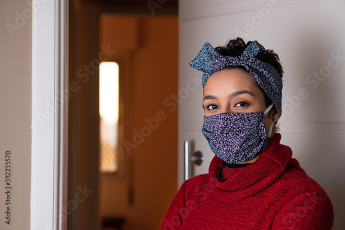 Portrait of serious african american womanwith matching headband and face mask looking at camera. At house entrance. Fashion, individuality, trend, Coronavirus or Covid-19 quarantine concept.