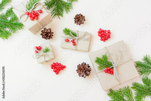 Christmas eco flat lay: gifts wrapped in craft paper, spruce branches and red berries as a decoration. Sustainability concept.