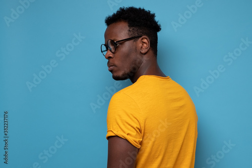 African man in glasses turning back. He is standing alone. Studio shot on blue wall.