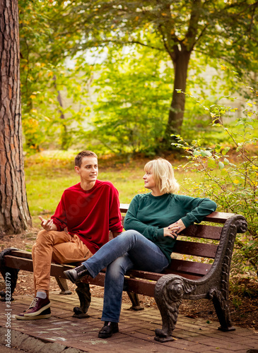 Beautiful woman,blonde,middle-aged,with a big son sitting on a wooden bench in a beautiful Park,Sunny day