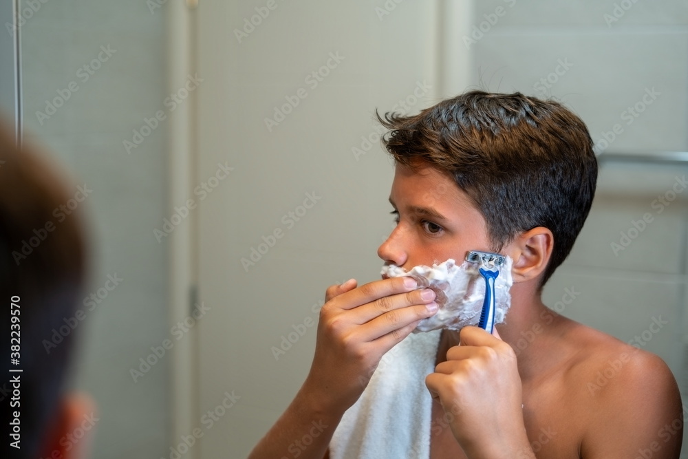 
Young man looking at himself in the mirror and shaving his beard with a razor