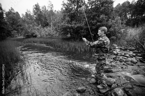  Fisherman standing on stones catching fish on the river. Black and white photography.