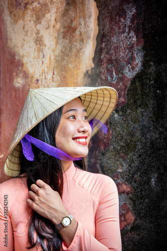 A young Vietnamese woman in a traditional Ao Dai dress and conical hat and smiling, Hue, Vietnam