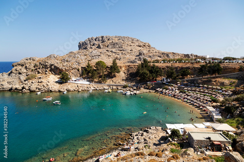 Sun shades line the beach at St. Paul's Bay on a sunny day in Lindos on Rhodes, Dodecanese, Greek Islands, Greece