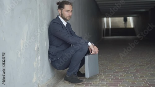Wallpaper Mural Side view of desperate businessman sitting down leaned against the wall in urban underground crossing. Depressed frustrated Caucasian handsome man with attache case thinking of his dismissal. Torontodigital.ca