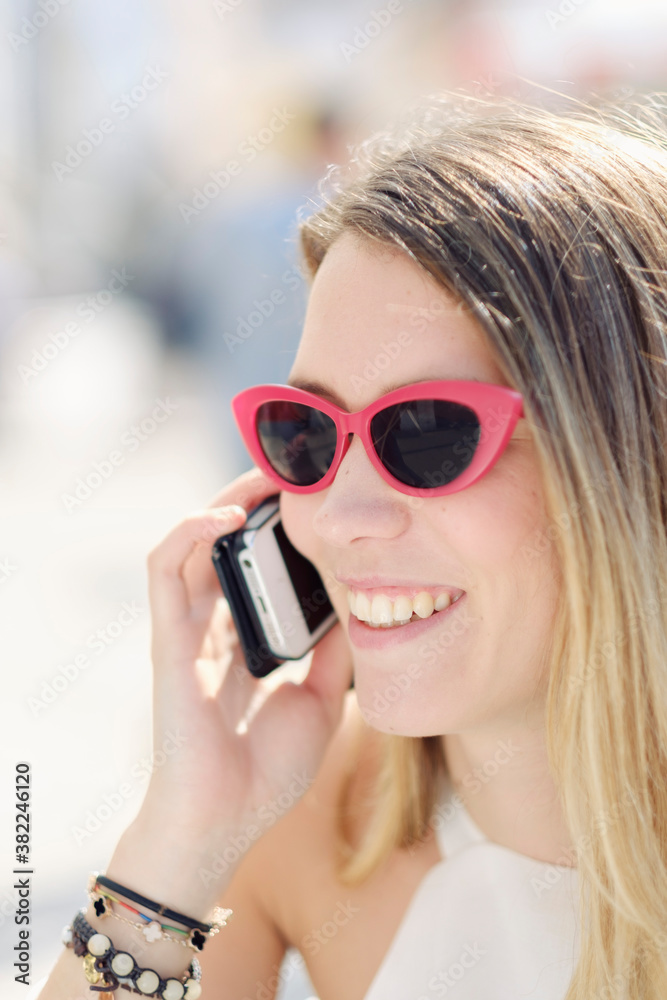 Headshot of a smiling young woman in sunglasses using her mobile phone outdoors, Portugal Headshot of a smiling young woman in sunglasses using her mobile phone outdoors, Portugal