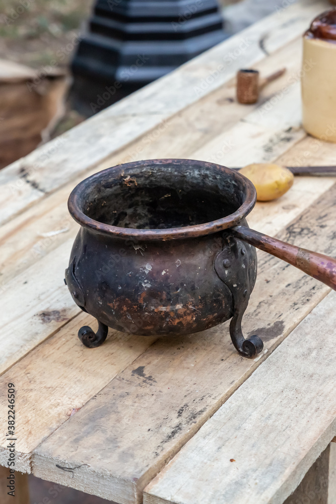 old mini bowler on a three-legged cast-iron pot stands on a wooden table, traditional kitchenware old mini bowler on a three-legged cast-iron pot stands on a wooden table, traditional kitchenware