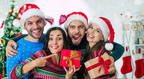 Happy group of excited beautiful friends in Santa hats are having fun while partying at home on the Christmas tree background