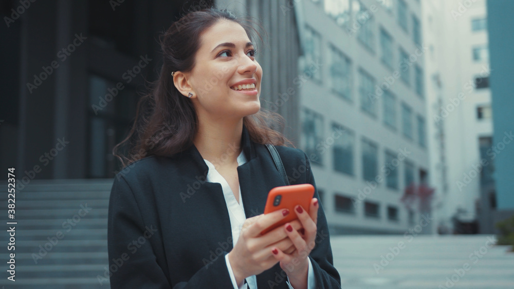 Young cheerful office girl caucasian pretty woman using smartphone networking social media while walking in business district outdoors. Carefree. Urban lifestyle. Young cheerful office girl caucasian pretty woman using smartphone networking social media while walking in business district outdoors. Carefree. Urban lifestyle.