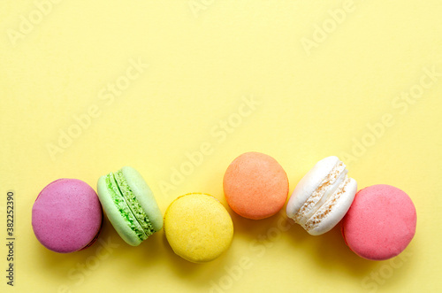 Sweet and colorful multicolored French macarons on a yellow background lined in a line, dessert with tea or coffee. place for text. view from above