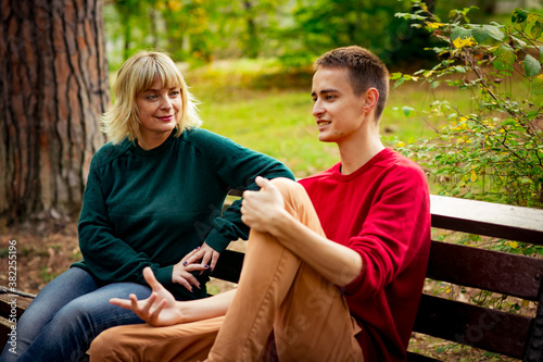 Beautiful woman,blonde,middle-aged,with her son,sitting on a bench and talking © khanfus