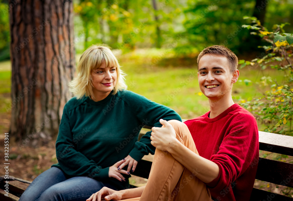 Beautiful woman,blonde,middle-aged,with her son,sitting on a bench and talking Beautiful woman,blonde,middle-aged,with her son,sitting on a bench and talking