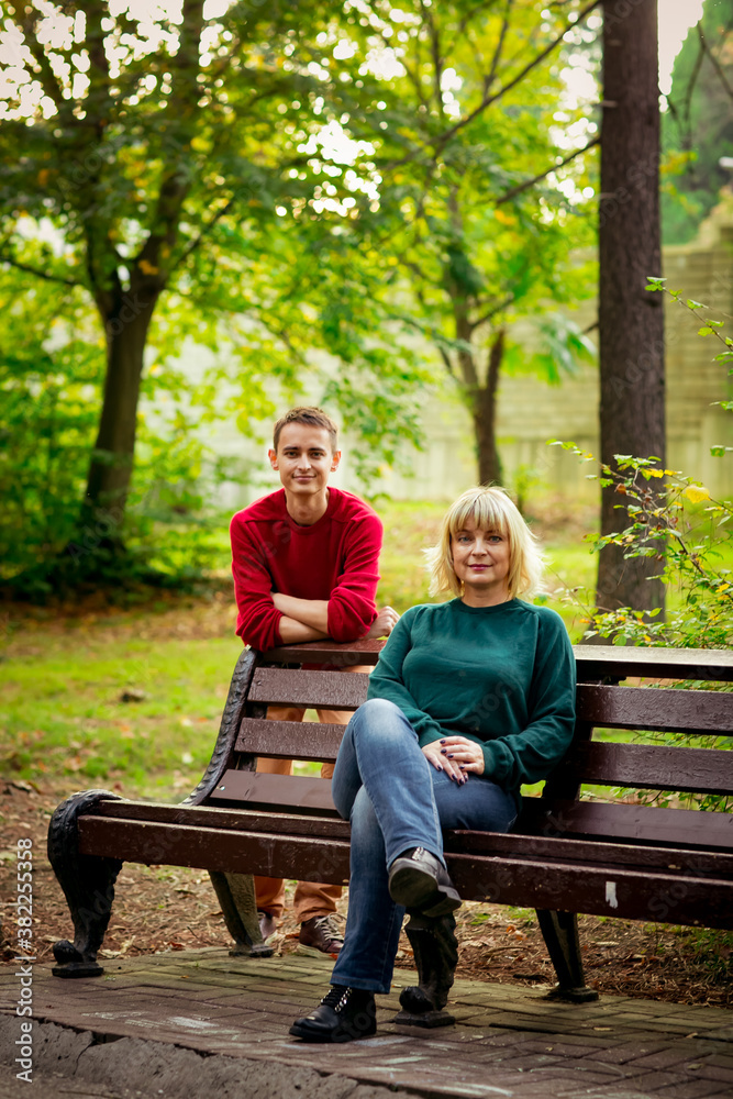 Beautiful woman,blonde,middle-aged,with her son,sitting on a bench and talking Beautiful woman,blonde,middle-aged,with her son,sitting on a bench and talking