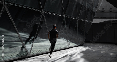 Male runner runs in city beside a glass architecture