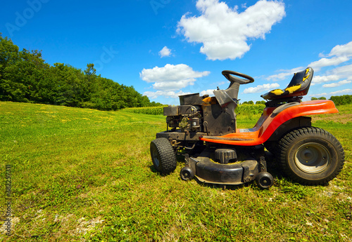 Old riding lawn mower at rest on a farm, wide angle.