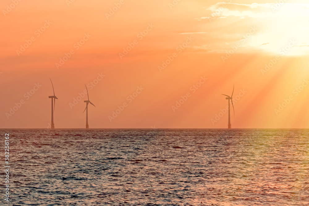 Offshore wind turbines. Pastel orange sunrise sky soft background. Peaceful spiritual image related to climate change and global warming.
