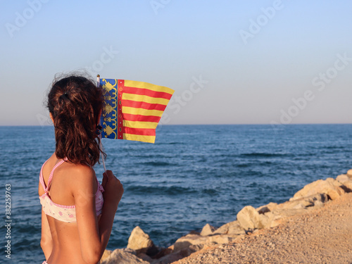 Girl on the beach with a flag in her hands

A girl holding a Spanish flag in her hands on the shore of the Bolar Sea in Spain Cullera, side view close-up. photo