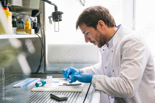 Side view of man in white coat sitting at table and examining samples while working in modern lab.