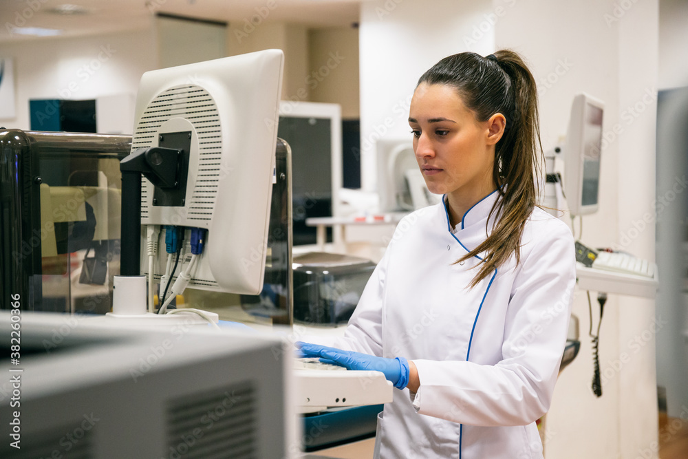 Pretty young woman in white apparel using sample analyzer while working in research lab.