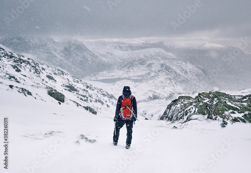 Winter mountaineer using Ice Axe and crampons below Great End. Esk Hause, Cumbria, UK.
