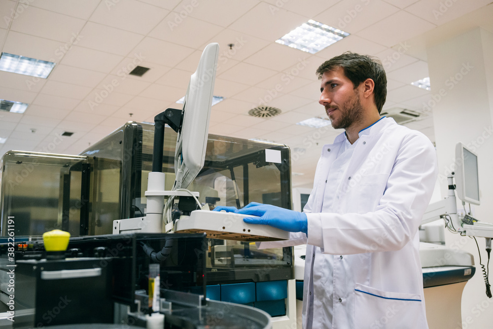 Side view of man in white coat using sample analyzer while working in ...