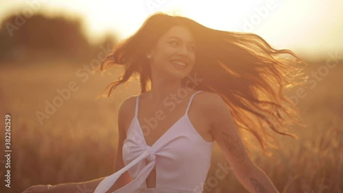 Smiling happy young dark-haired Caucasian woman spinning around in the field among dry wheat spikelets. Joy concept