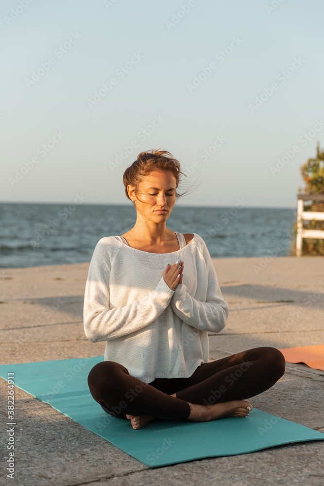 Solitary barefooted woman meditating in lotus pose on waterfront during sunrise Solitary barefooted woman meditating in lotus pose on waterfront during sunrise