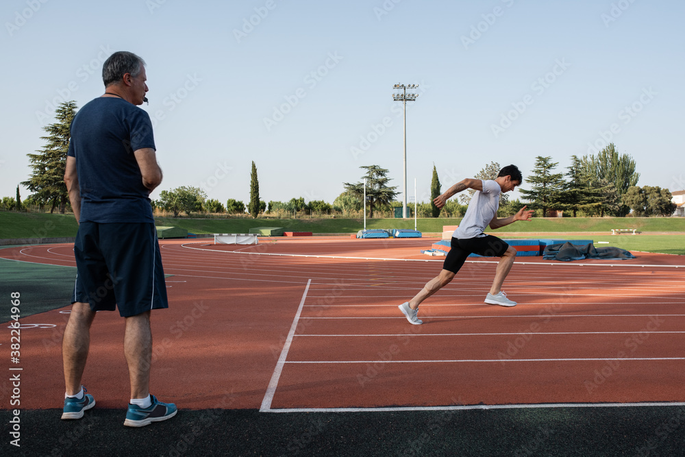 Trainer supervising running athlete on track Trainer supervising running athlete on track