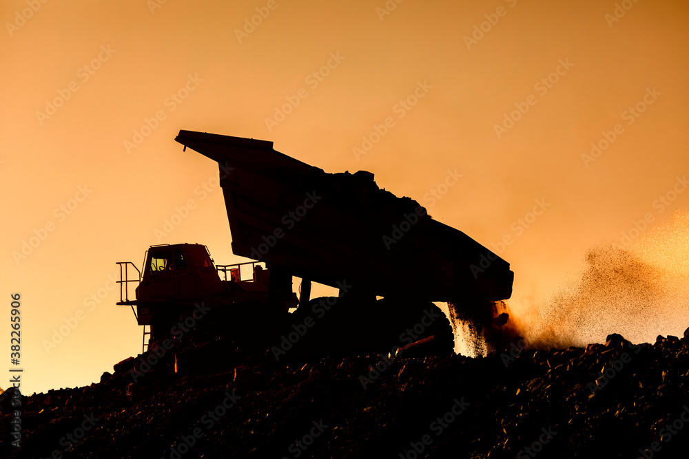 A very large haul dump truck at a construction site in Silhouette against an orange sky