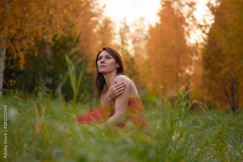 beautiful young woman in red dress sitting in autumn forest.