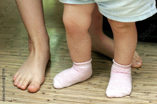 Baby's first steps. Small and large feet close-up. Teach your child to walk. The concept of proper physical development of the child. Small children's feet in socks take the first steps