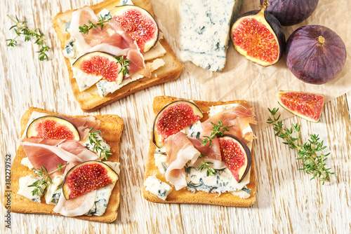 Open sandwich with blue cheese, prosciutto and fresh figs on a white table, top view.