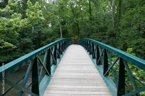 Wooden footpath bridge with metal handrails crossing creek through forest perspective