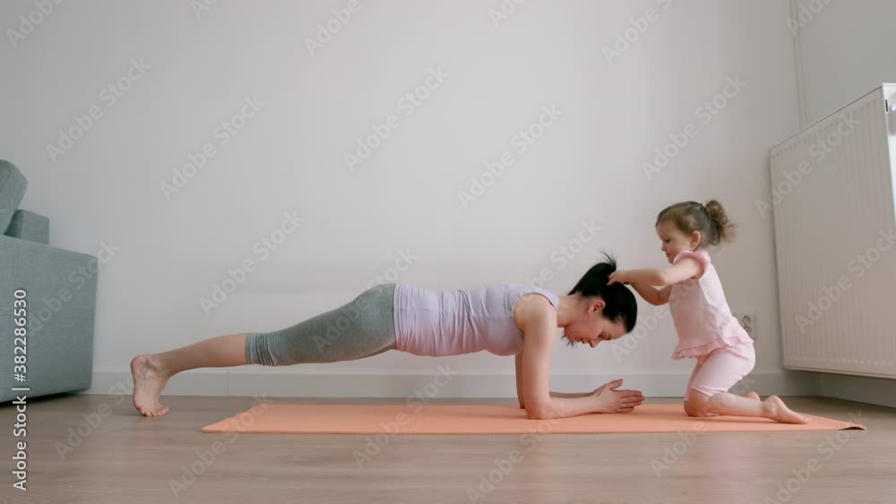 Mother in plank exercise and little girl plays with her mother's hair at home