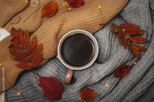 autumn, dry red autumn leaves lie on sweaters that are stacked around a hot espresso mug, around lies a led garland, Flatley