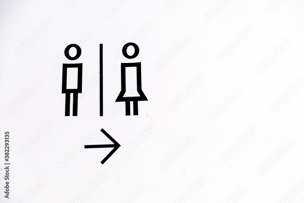 Fototapeta premium Toilet sign with simple black icon of male and female with arrow pointing to the right against white concrete wall. 