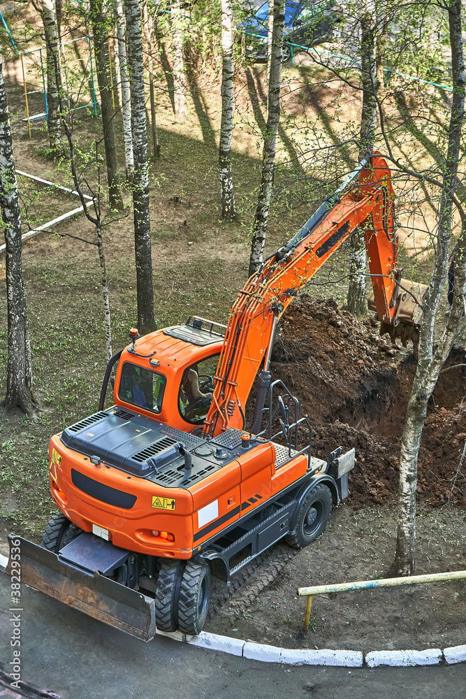 Mini excavator digging a trench among the trees for repairing city communications