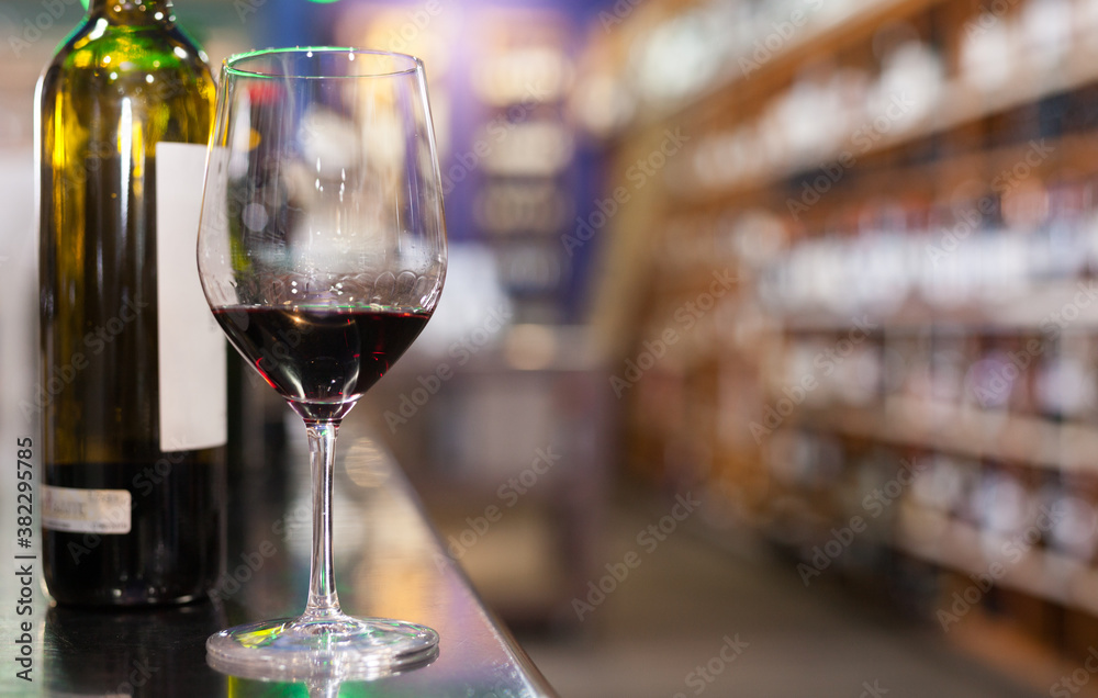 Red wine tasting glass and wine bottles against blur background of wine store interior..