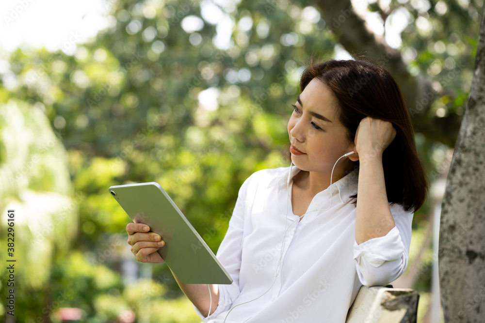 Portrait of a smiling young business woman using tablet for watching movies and listening music in the park with earphones. Changing workplace to create creative ideas and new ideas. Portrait of a smiling young business woman using tablet for watching movies and listening music in the park with earphones. Changing workplace to create creative ideas and new ideas.