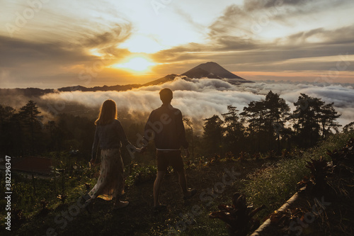 A loving couple man and woman walking near Batur volcano. Back view. Hold hands. Sunrise. Sunset. Tourists lovers on honeymoon enjoying summer vacation. Travel bloggers. Bali landmark
