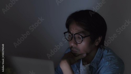 Truck Shot Asian Casual Businessman or Freelance in Jeans Shirt Wear Glasses Typing Laptop Touch Chin and Working Late at Office in Normal View
